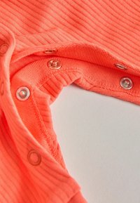 Gros plan d'un tissu côtelé corail avec des boutons-pression en métal fermés et ouverts le long d'un bord courbe sur un fond clair.