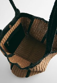 Gevlochten stro tote bag met zwarte geweven handvatten, met een ruime binnenkant en een extra zwart ritsvak.