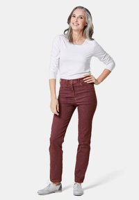 Chemise blanche à manches longues, jeans bordeaux taille haute, portés avec des chaussures oxford grises. Présente une coupe ajustée et une texture denim classique.