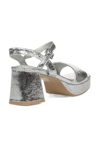 Sandalias de tacón alto metálicas plateadas con un acabado texturizado, punta abierta, correa ajustable en el tobillo y un tacón cuadrado grueso.