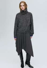 Szürke kötött garbó texturált kivitelben, egy áramló szürke aszimmetrikus szoknyával és elegáns fekete, hegyes orrú csizmával párosítva.