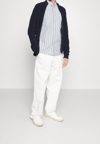 Námořnický žebrovaný cardigan přes světle modrou proužkovanou košili s knoflíky, spárovaný s bílými širokými kalhotami a bílými teniskami.