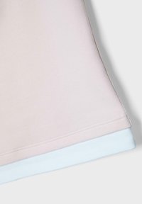 Tissu rose clair superposé à un tissu blanc, montrant des bords cousus et une texture lisse sur un fond neutre.