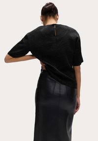 Donna con un bun intrecciato che indossa un top corto nero testurizzato e una gonna in pelle nera a vita alta, mostrata di spalle.