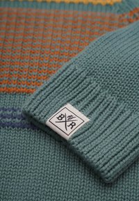 Stickad tröja med en teal kropp och orange, gula och lila ränder. Texturerad tyg med ribbad manschett och en etikett med "BXR".