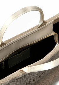 Beige handtas met textuur en stoffen handvatten, open ritssluiting met zwarte binnenkant en een klein binnenvakje.