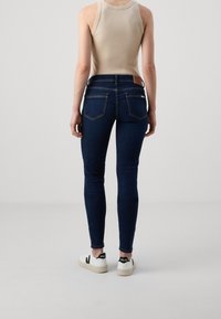 Tajta jeans i mörkblå denim med medelhög midja, bakfickor och en slät textur. Bärs med vita sneakers.