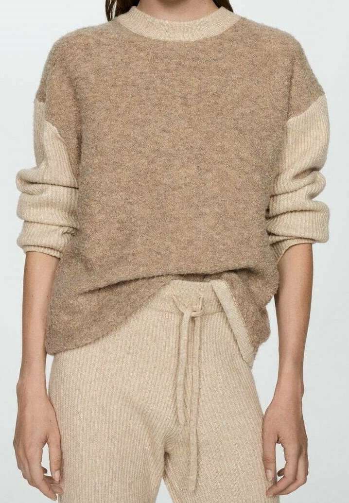 Femme portant un pull texturé beige et marron clair avec des manches côtelées, associé à un pantalon beige côtelé avec cordon de serrage.