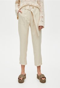 Pantalon beige taille haute avec une poche frontale, passants pour ceinture et une ceinture en tissu. Caractéristiques : revers roulés et coupe droite décontractée.
