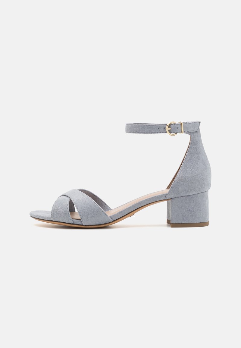 Sandale à talon bloc en daim bleu clair, à bout ouvert, avec bride à la cheville et boucle dorée, présentée de profil sur un fond uni.