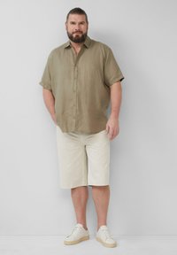 Helle braune Kurzarmbluse aus Leinen mit Knopfverschluss, kombiniert mit cremefarbenen Shorts und weißen Sneakers mit braunen Akzenten.