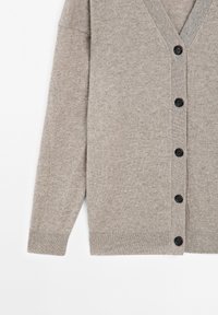 Grå stickad kofta med V-urringning, långa ärmar och framknäppning med sex svarta knappar. Mjuk textur och avslappnad passform.