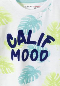 Balta medvilninė marškinėliai su žaliais ir mėlynais tropiniais lapų raštais, šalia yra užrašas "CALIF MOOD" tamsiai mėlynomis didžiosiomis raidėmis.