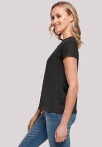 Black short-sleeve t-shirt made of cotton, featuring a relaxed fit and round neckline, displayed on a smiling model in profile.