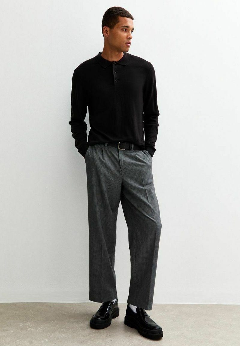 Polo shirt nero a maniche lunghe con tre bottoni, abbinato a pantaloni grigi a scacchi e scarpe con plateau nere. Tessuto testurizzato, vestibilità comoda.