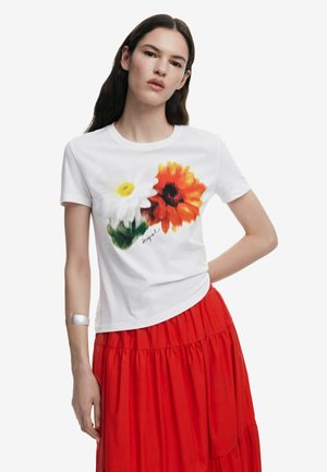 T-shirt bianco a maniche corte con stampa floreale che presenta una margherita gialla e un girasole arancione. Il design include una firma scritta a mano.
