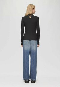 Zwarte langemouwtop met een ronde sleufdetail op de rug, gecombineerd met lichtblauwe wijde jeans met een rafelige zoom.