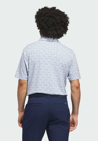 Golfpolo i lyseblå med et gentagende abstrakt mønster i rød og marineblå. Kortærmet med krave, kombineret med marineblå bukser.