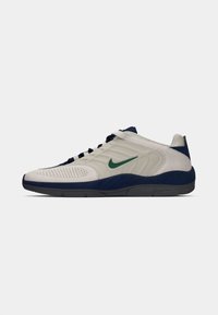 Grå tekstil sneakers med en marineblå såle, med en grønn Nike swoosh, perforert overdel for pusteevne, og tradisjonelt snøresystem.