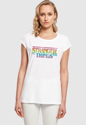 Hvit bomulls T-skjorte med rullede ermer, prydet med flerfargede rhinsteinbokstaver som sier "STRANGER THINGS." Avslappet passform, rund hals.