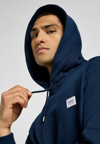 Sudadera con capucha de color azul marino con un acabado texturizado, cordón en el cuello y un parche blanco con el logo de Lee en el pecho.