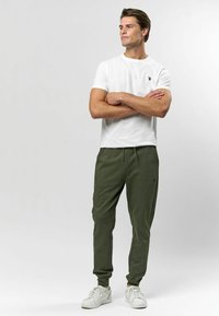 Biela bavlnená tričko s krátkymi rukávmi v kombinácii so zelenými teplákmi s elastickým pásom a manžetami na členkoch. Biele tenisky.