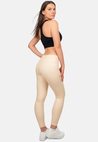 Top corto nero e leggings beige, realizzati in tessuto elasticizzato. I leggings presentano una vita senza cuciture e una texture liscia. Sneakers bianche indossate.
