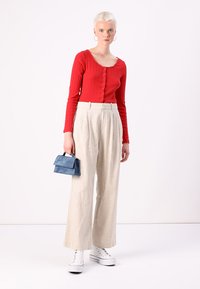 Haut rayé rouge à manches longues avec des détails de boutons, pantalon large crème, et un petit sac à main bleu. Des baskets blanches complètent le look.