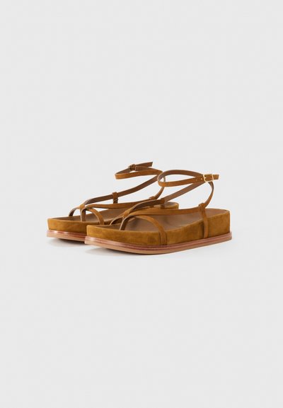 Bruna mockaskor med platta sulor och flera tunna remmar. Har en minimalistisk design med rund tå och en lätt trädetalj på sulan.