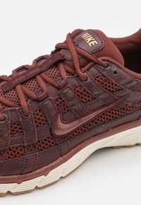 Närbild av en vinröd Nike Air-sko med detaljer i mesh och mocka, bruna snören och vit ribbad sula.