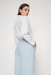 White long-sleeve button-up shirt with a yoke detail, paired with light blue high-waisted trousers featuring side pockets and a smooth texture.