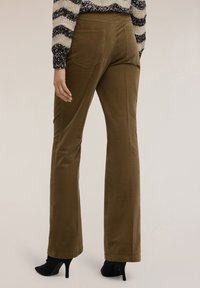 Hnědé kordové kalhoty s rozšířenými nohavicemi a hladkou strukturou, doplněné o dvě zadní kapsy, v kombinaci s černými lodičkami a pruhovaným svetrem.