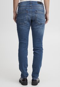 Slim-fit sinised teksad, millel on sile tekstuur, kaks tagataskut, diskreetne oranž õmblus ja must vöömärk.