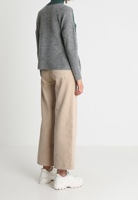 Pull gris en maille avec texture côtelée, associé à un pantalon beige à jambes larges et des baskets blanches épaisses. Détails de coutures visibles et coupe décontractée.