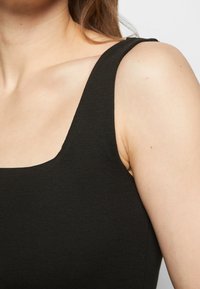 Femme portant un débardeur noir côtelé sans manches, montrant l'épaule, la clavicule et le cou.