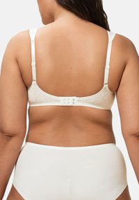 Crèmekleurige bh met verstelbare bandjes, bloemmotief en vierhaakssluiting aan de achterkant. Glad stof met subtiele glans en afgeronde cups.