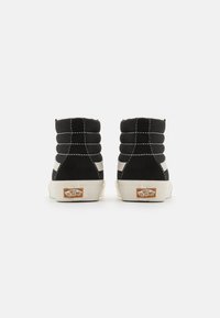 Zapatillas negras de corte alto hechas de material de ante, con un cuello acolchado y franjas de cuero blanco en contraste. Suela de goma color crema con un parche del logotipo en el talón.