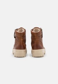 Bottines en cuir marron avec une finition texturée, semelle épaisse de couleur claire et fermeture éclair sur le côté. Doublure douce visible en haut.