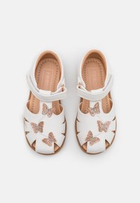 Valkoiset nahkasaappaat, joissa on leikattu muotoilu, ruusukultaiset perhoskoristeet, säädettävä hihna ja vaaleanbeige sisävuori.