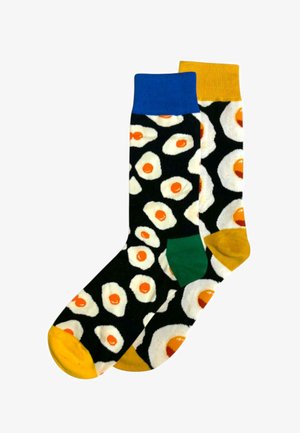 Gambe con calzini neri bordati di giallo, con talloni e punte decorati con un motivo di uova fritte.