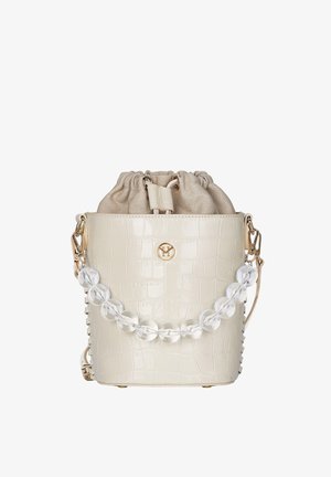 Femme en robe vert olive tenant un sac seau beige avec des anses en perles transparentes, portant des sandales noires à talons hauts.