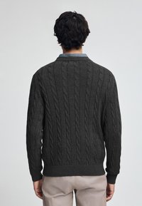 Dunkelgrauer Kabelstrickpullover mit gerippten Bündchen und Saum. Verfügt über einen kragenförmigen Ausschnitt und ein strukturiertes Muster. Das Modell ist von hinten zu sehen.