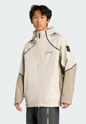Light beige waterproof jacket with hood, contrasting tan sleeves, zip front, and grey accents. Features logo on chest and sleeve.