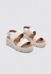 Sandalias de plataforma blancas con dos correas anchas, cierre de hebilla y plantilla contorneada marrón. Fabricadas en material sintético con una textura suave.