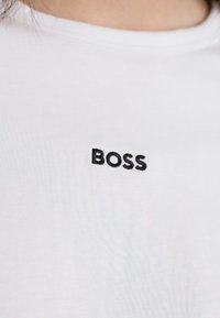 Bílá bavlněná tričko s malým černým vyšitým logem "BOSS" na oblasti hrudníku. Jednoduchý design s kulatým výstřihem.