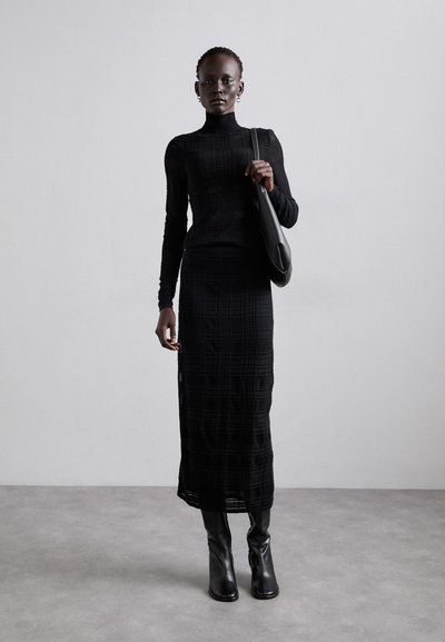 Top negro ajustado de manga larga hecho de tela texturizada, combinado con una falda bodycon negra con un patrón de cuadrícula y botas negras hasta la rodilla.