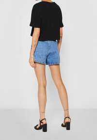 Svart kortärmad t-shirt, korta blå denimshorts med slitna kanter, svarta klacksandaler med blockklack, synliga tatueringar på armarna.