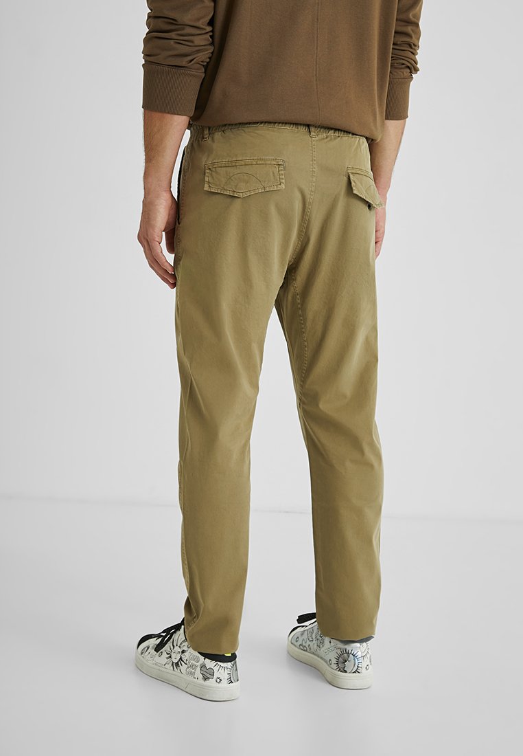 Olivegrüne, leichte Hosen mit entspannter Passform, elastischem Bund, Rückentaschen und strukturierter Textur; kombiniert mit gemusterten Sneakers.