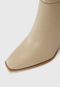 Beige Leder-Ankle-Boot mit spitzer Zehenform, glatter Textur und niedrigem gestapeltem Absatz, mit minimaler Naht und schlanker Silhouette.