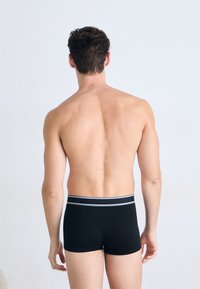 Boxers noirs avec une taille douce présentant des accents blancs, vus de l'arrière. Matière lisse sans motifs ni détails visibles.